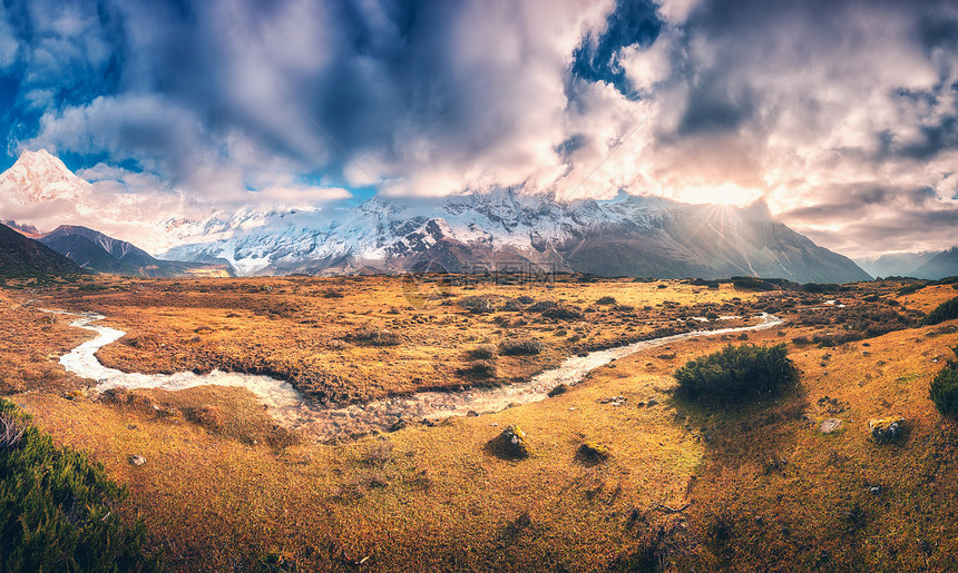 全景景观与雪覆盖的山峰紫色的云,太阳,小河,橙色的草,蓝天日出五颜六色的风景与草地,小溪,雪岩尼泊尔的秋天图片
