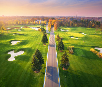 比利茨基秋天日落时穿过高尔夫球场秋季巷道绿色高尔夫球场的鸟瞰图景观与路线,草地,绿色松树,橙色森林,美丽的天空看背景