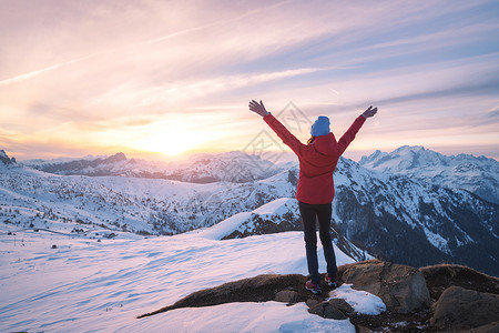快乐的轻女人雪山日落冬天美丽的苗条女孩山峰上举手臂,雪覆盖着岩石五颜六色的天空白云岩中旅行旅游业背景图片