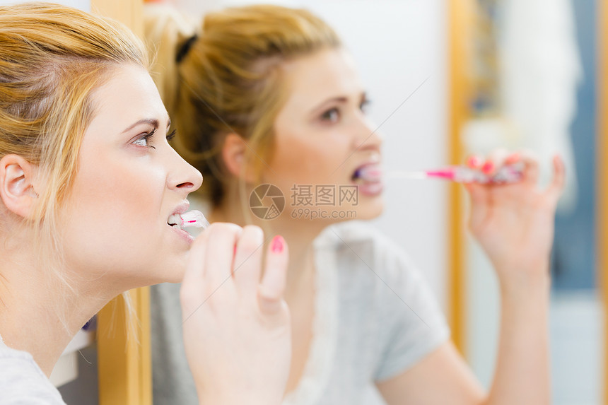女人刷牙特写浴室里带牙刷的金发女孩,看着镜子口腔卫生女人浴室刷牙图片