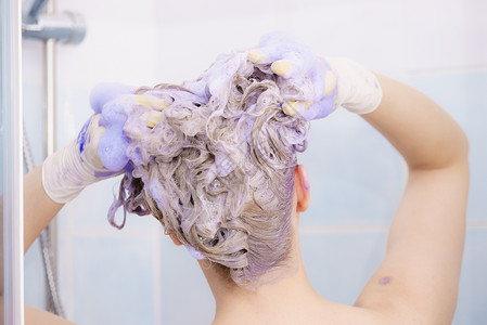 泡沫头女人头发上涂上着色洗发水紫色洗涤产品的女家里涂金色女人头发上涂墨粉洗发水背景