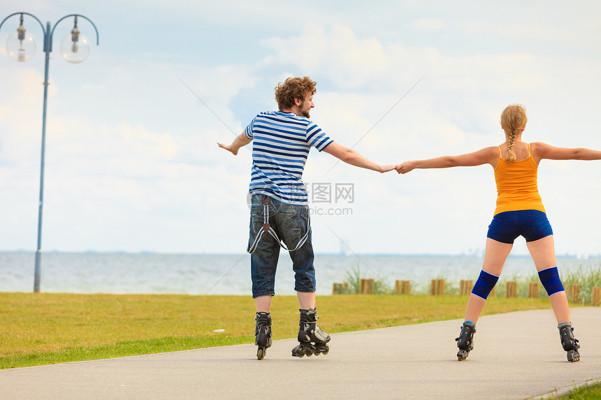 节日,积极的人友谊的轻的穿着溜冰鞋的夫妇骑海边的户外,女人男人长廊上滑行图片