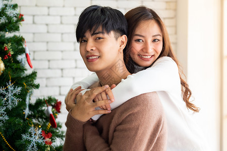 轻的亚洲成青少夫妇拥抱庆祝诞节,客厅与诞树装饰装饰图片