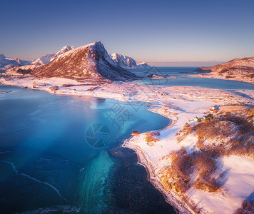 日落时,雪覆盖着山脉房屋清澈的水蓝天冬季景观与海岸,雪岩,罗布,道路挪威洛福滕群岛小村庄的顶部景观背景图片