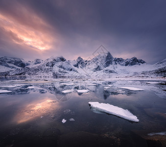 雪山,蓝色的大海霜冻的海岸,挪威洛芬岛五颜六色的日落时,水多云的天空中反射冬天的风景雪覆盖的岩石,晚上冰的峡湾背景图片
