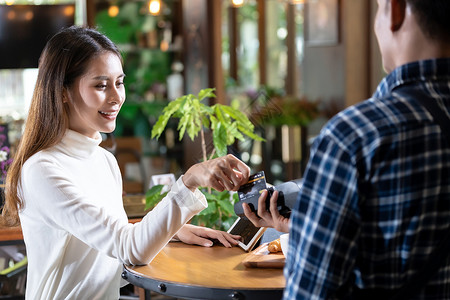 亚洲女客户用信用卡刷卡器EDC机器支付服务员咖啡馆的桌子上购买咖啡背景