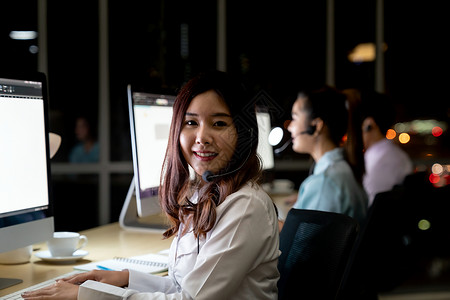 亚洲轻成人信心运营商女代理与耳机工作呼叫中心的夜间环境与他的同事队客户服务技术支持用深夜努力工作24小时背景图片
