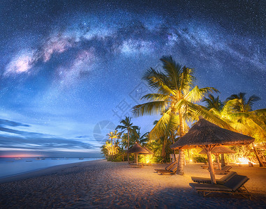海滩在晚上在沙滩上流淌着奶水夏季晚上有绿棕榈树防晒床和雨伞海滨风景美丽的蓝星空和银河系在桑给巴尔非洲空间旅行背景