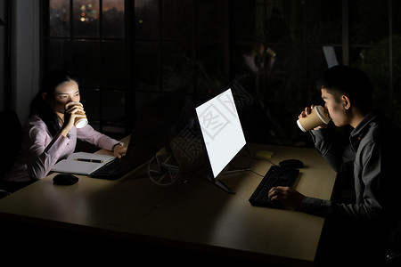 成年亚洲青商人和女商人晚上在办公室用台式电脑和笔记本工作时喝热咖啡图片