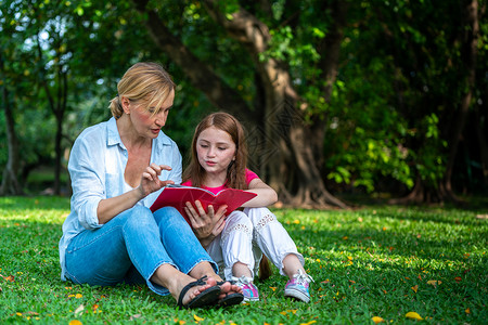 户外公园中母女在草地看书成熟高清图片素材