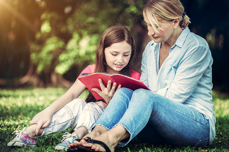 户外公园中母女在草地看书教育高清图片素材