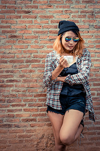 快乐的年轻时髦女人站在街上砖墙旁边手里拿着咖啡杯站立高清图片素材