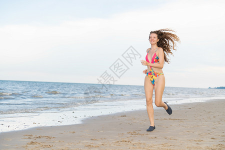 夏季年轻女跑步者身穿比基尼在热带沙滩上奔跑图片