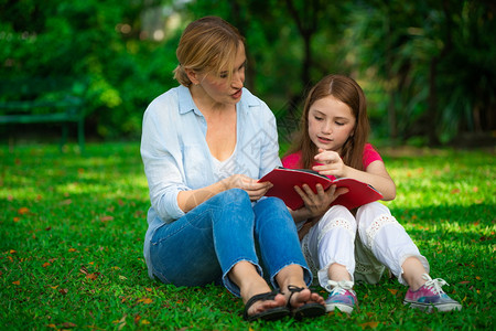 户外公园中母亲和孩子在草坪上看书阅读教育高清图片素材