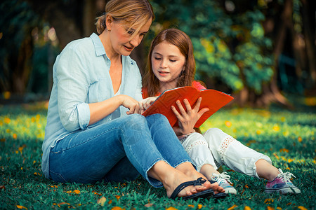 户外公园中母亲和孩子在草坪上看书阅读文学高清图片素材