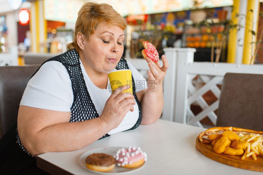 胖女人在快餐厅吃甜圈不健康的食物胖女人在餐桌上吃垃圾晚饭肥胖问题女人在快餐厅吃甜圈图片