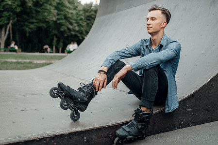年轻男子穿着轮滑鞋坐在轮滑板上休息背景图片
