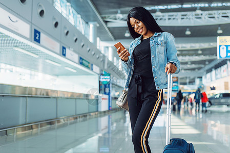 携带手提箱和电话等待在国际机场启程的黑人女游客图片