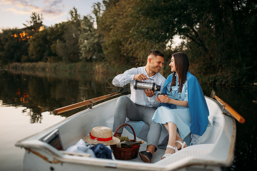 在日落时宁静的湖边一条船上爱对夫妇和热水船浪漫的聚会划船旅行男人和女沿河行走在宁静的湖边一条船上爱对夫妇和热水船图片
