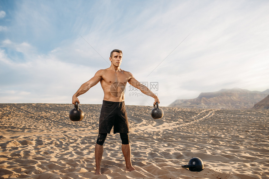 在沙漠上双手分开提着壶铃的肌肉男图片