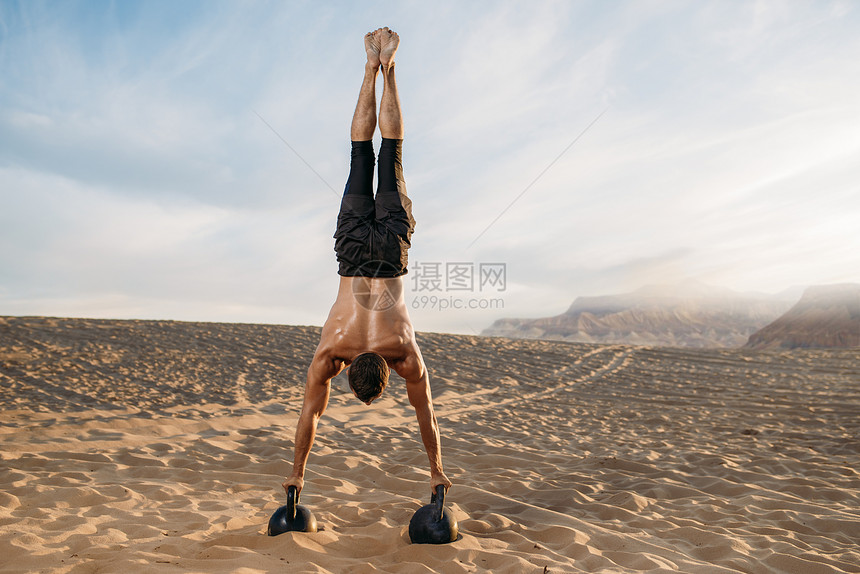 在沙漠上双手握着壶铃倒立的肌肉男背面图片