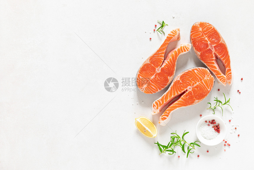 新鲜生鲑鱼牛排配有烹饪原料草药和白底柠檬顶视图片