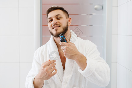 穿浴袍的男子在浴室用电动剃刀刮胡子图片