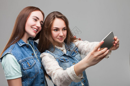 两个笑着的女友穿牛仔夹克在工作室用手机自拍图片
