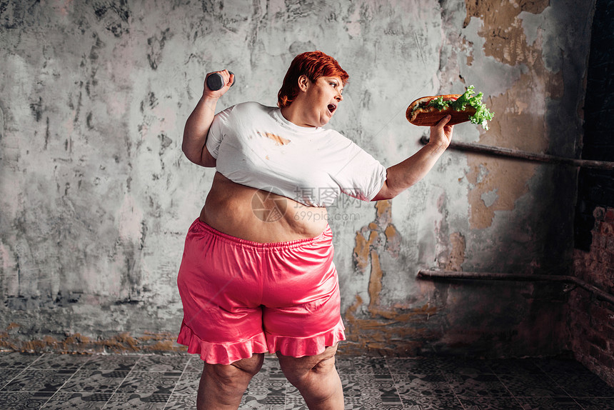 超重的女人手里拿着哑铃和三明治对抗肥胖的观念超重的问题吃垃圾食品超重女对抗肥胖观念图片