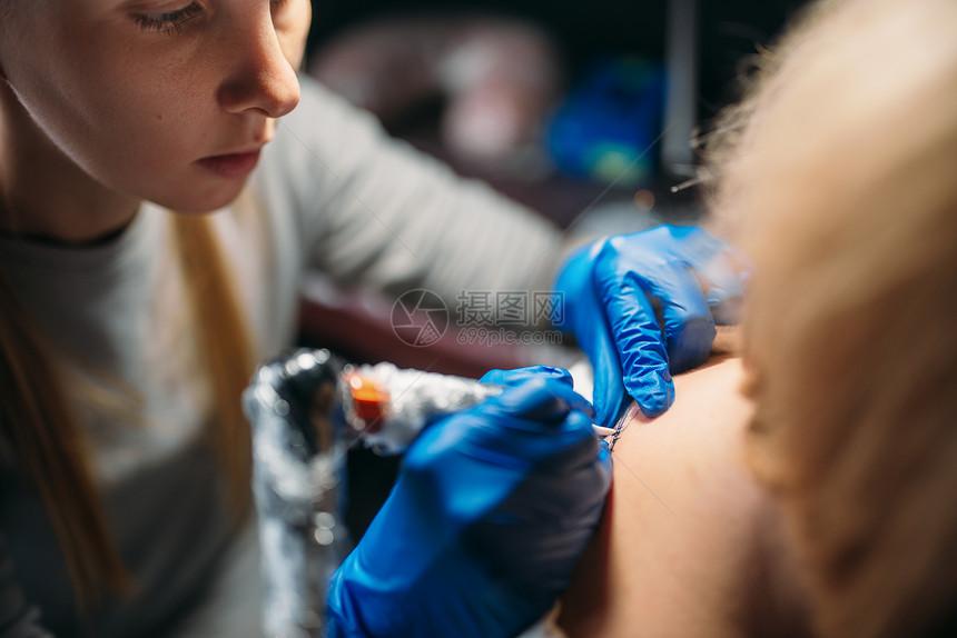 蓝无菌手套上的女纹身者做机器沙龙大师工作室的专业纹身过程图片
