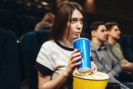 有饮料和爆米花的年轻女子坐在电影院表演时间看电影图片
