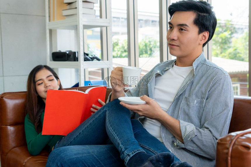 女子坐在沙发上的看书男子喝咖啡图片