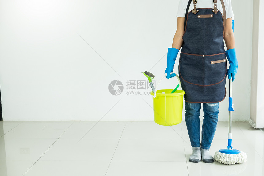 年轻女管家在离开室的房屋地板上打扫用拖把和塑料桶刷子手套和洗涤剂清拖和塑料桶帮助妻子图片