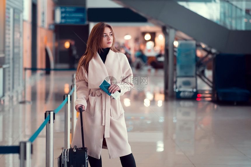 年轻女孩拿着行李箱站在机场扶梯旁图片