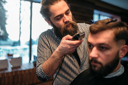 理发师用剪机做理发师上面印着黑沙发披风的客户男子发型以背景为的理发店图片
