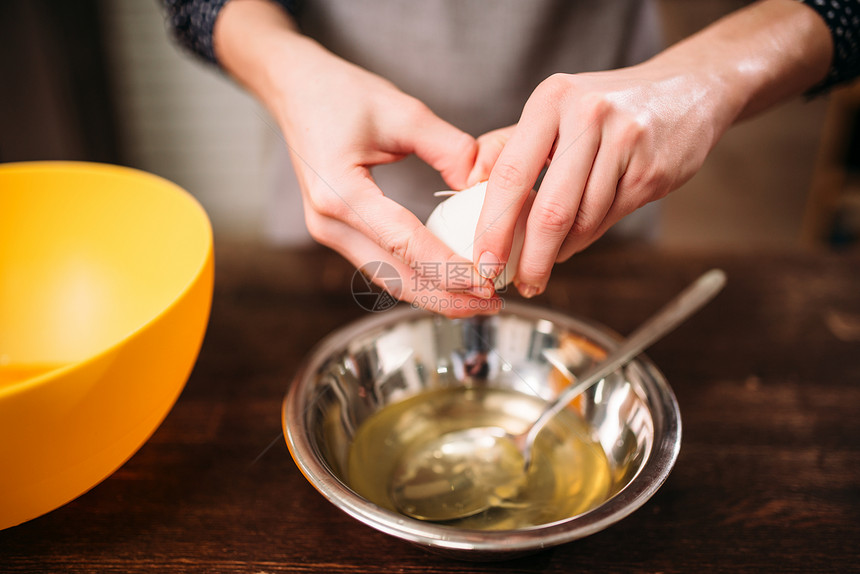 女人的手把鸡蛋打碎在木桌上的碗里图片