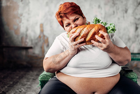超重的女人坐在椅子上吃三明治食图片
