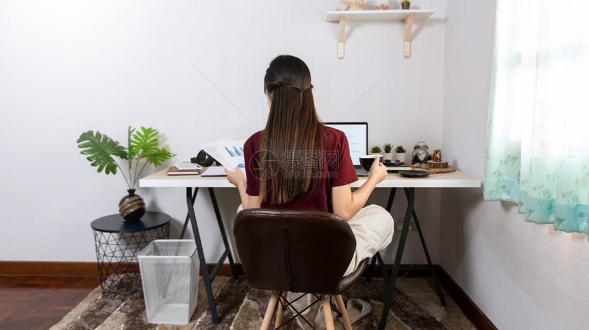在室内客厅办公作为自由职业者电子协调工作远程或在家以外的概念而使用笔记本电脑和文件的年轻有吸引力漂亮亚洲女图片