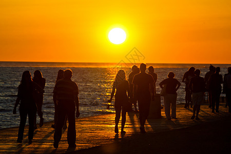 夕阳西下成群的人们在海边漫步图片