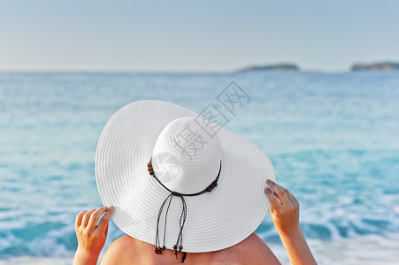 一个女人在沙滩的甲板椅子上晒日光浴握着手帽天空高清图片素材