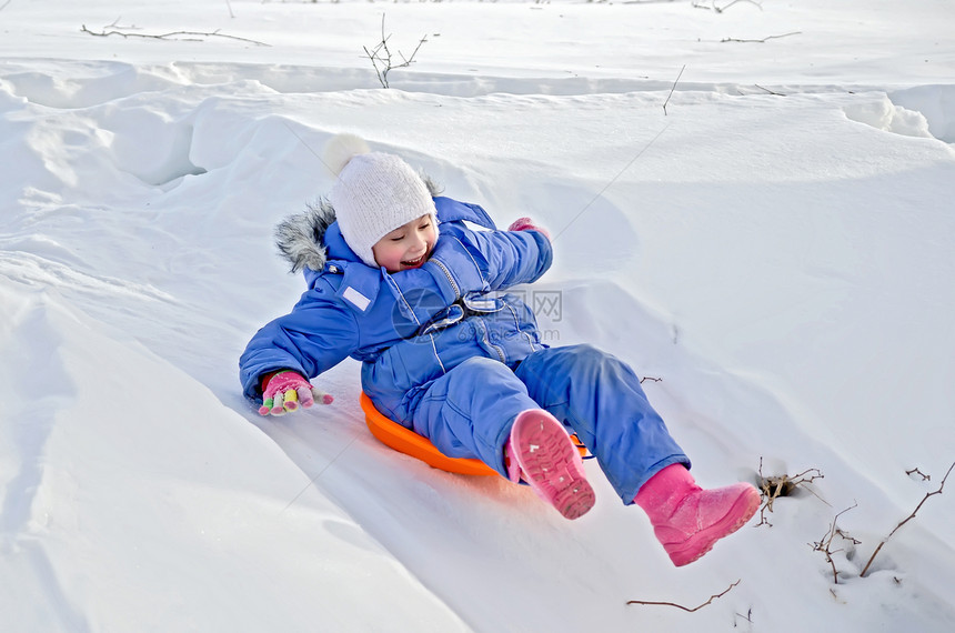 小孩在冬天雪中​从雪橇上滑下山丘图片