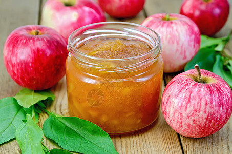 苹果果酱玻璃罐中的苹果酱新鲜红苹木板上叶子的树枝背景
