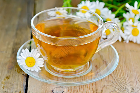 玻璃杯中的草药茶木板背景上鲜的甘菊花背景图片