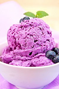 蓝莓冰淇淋夹薄荷和浆果碗里底有紫布和木板高清图片