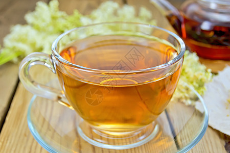 从玻璃杯和茶壶中摘取的草药和茶壶中叶纸上草药和茶壶的干鲜花木板背景上的草药和鲜花药用高清图片素材