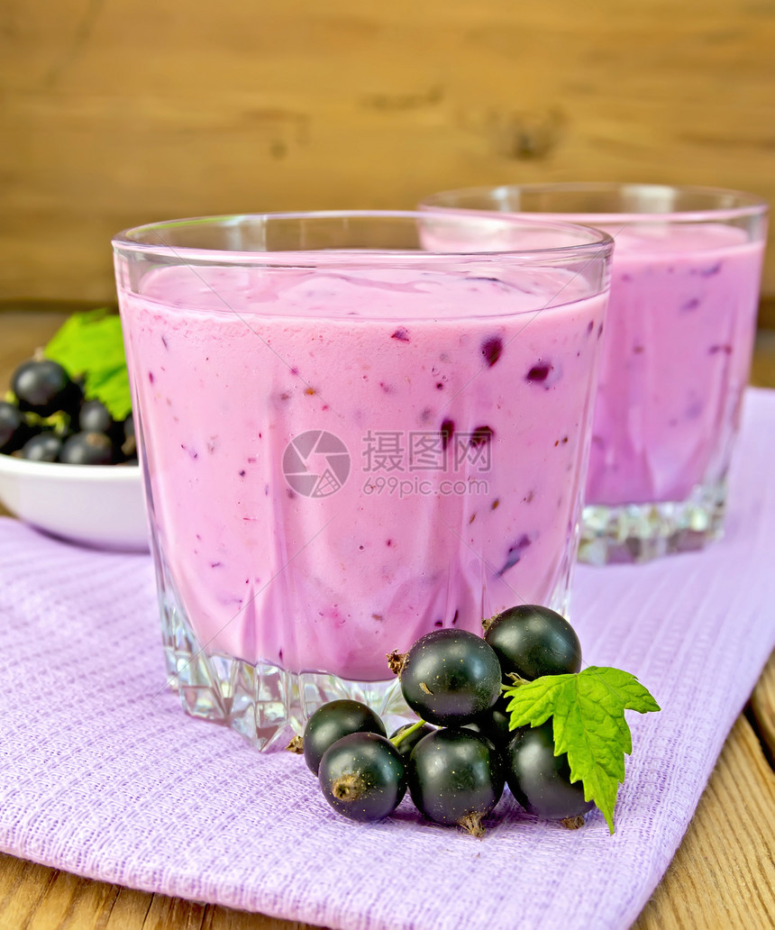 紫色餐巾纸上两个低杯子罐中黑色的奶昔木板背景上有浆果卷子的碟图片