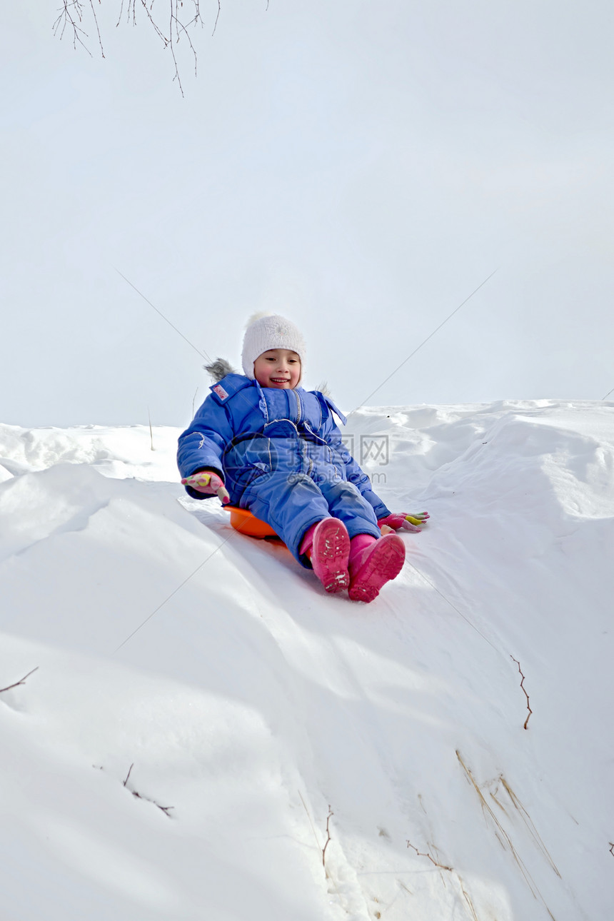 小女孩在雪橇上滑下山坡在冬天雪图片