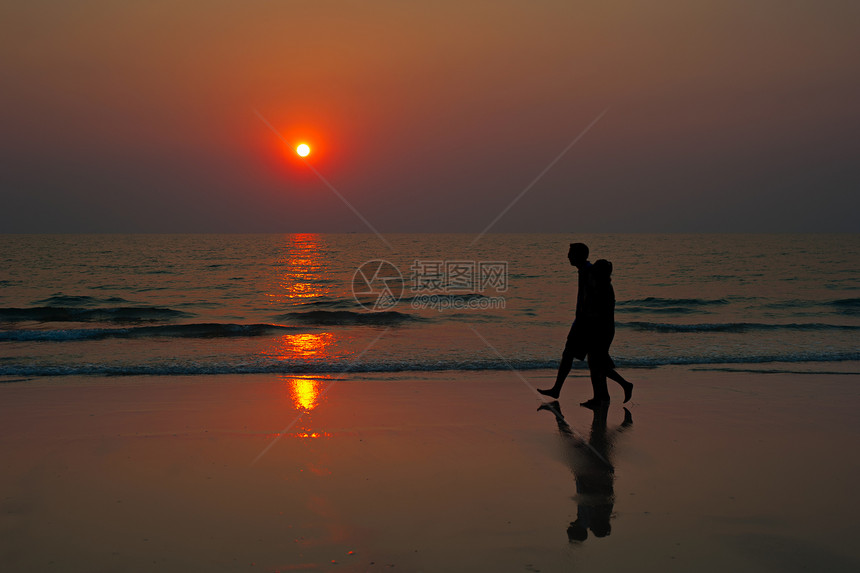 日落时在海滩上散步的情侣图片