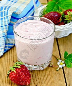 草莓和酸奶玻璃中的奶昔白柳篮中的草莓花和叶子以及木板上的餐巾纸背景