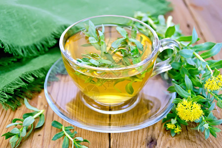 玻璃杯中的草药茶配有鲜花木板上的绿布罗迪奥拉玫瑰花金色的高清图片素材